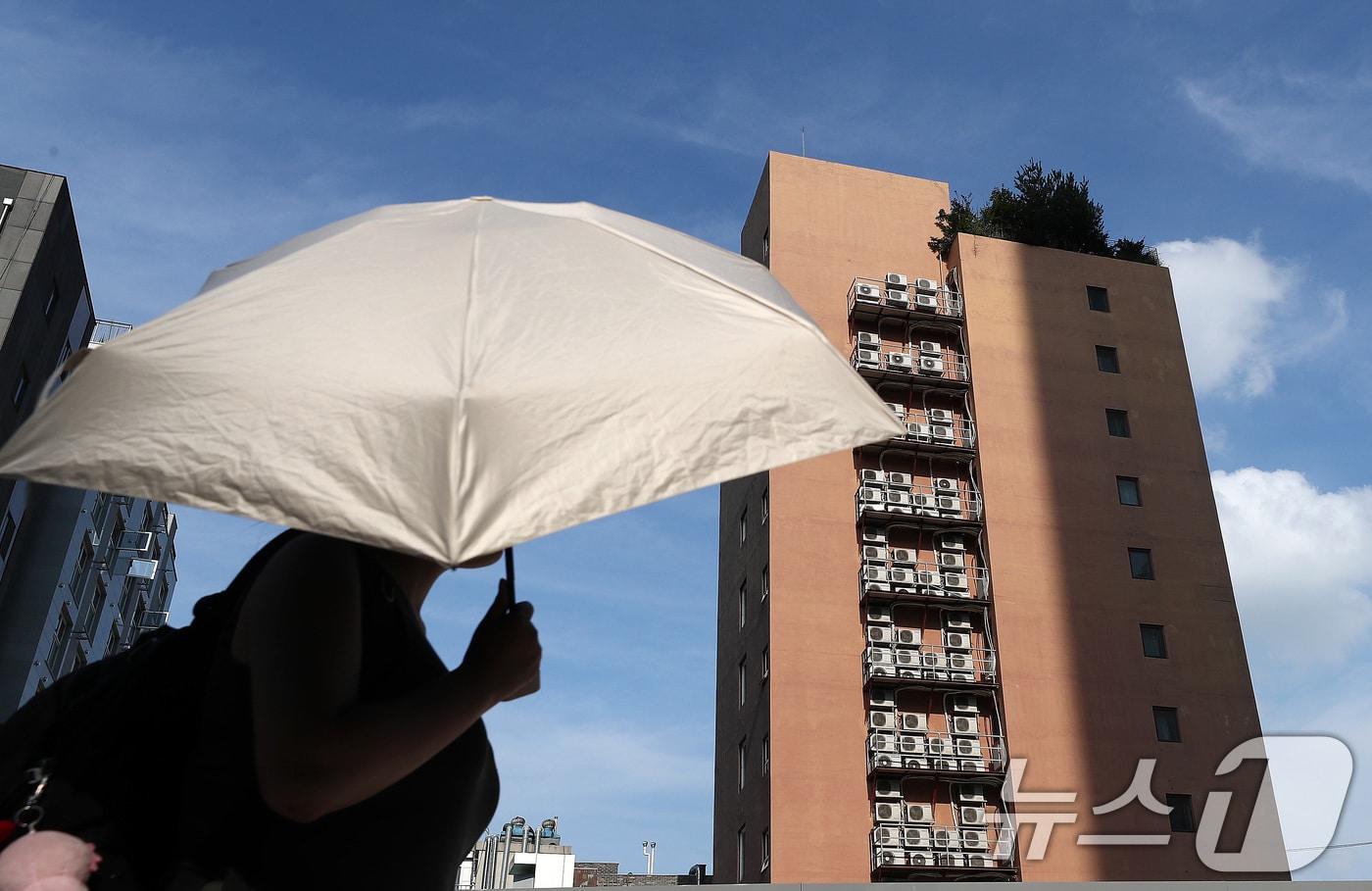 8일 서울 종로구의 에어컨실외기가 밀집된 한 건물외벽 앞으로 양산을 쓴 한 시민이 지나가고 있다.ⓒ News1 박세연 기자
