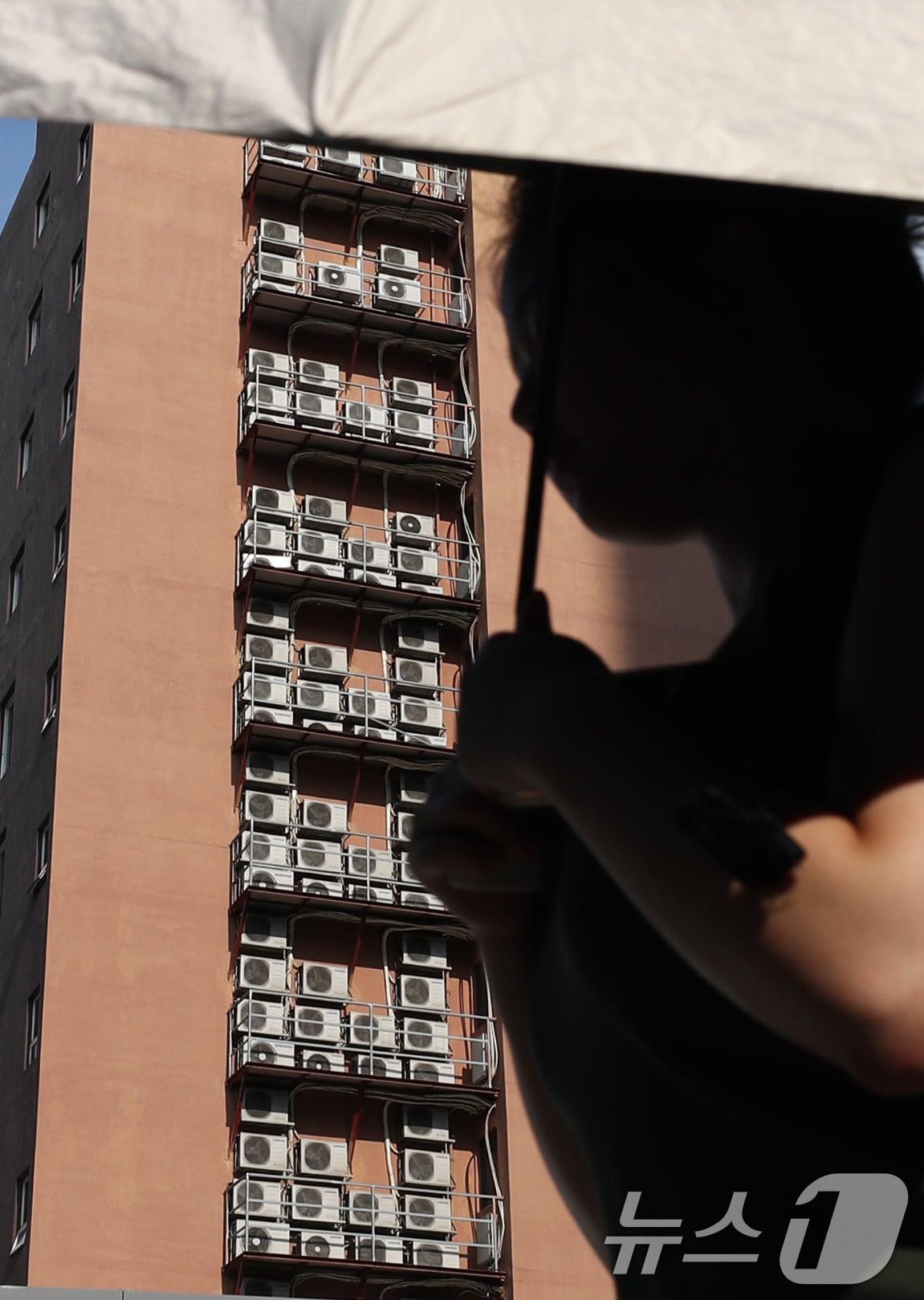 본문 이미지 - 에어컨실외기가 밀집된 한 건물외벽 앞을 한 시민이 지나가고 있다. 2024.8.8/뉴스1 ⓒ News1 박세연 기자
