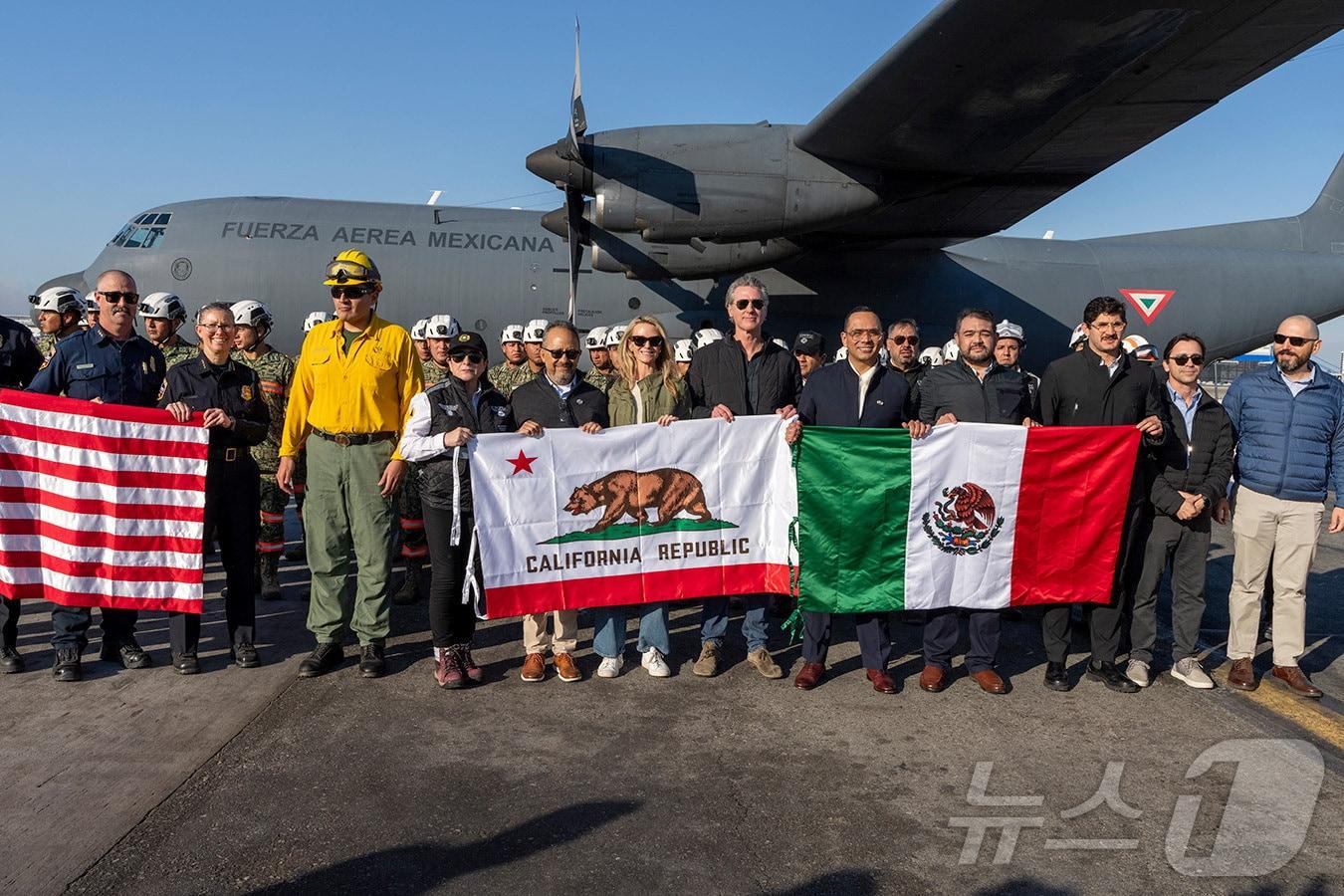 본문 이미지 - 11일(현지시간) 미국 캘리포니아주 로스앤젤레스(LA)에서 개빈 뉴섬 캘리포니아 주지사와 LA산불 진압을 위해 멕시코에서 파견된 소방관들이 캘리포니아 깃발과 미국, 멕시코 국기를 들고 기념촬영을 하고 있다. 사진은 개빈 뉴섬 주지사실 제공. 2025.01.11 ⓒ 로이터=뉴스1 ⓒ News1 김지완 기자