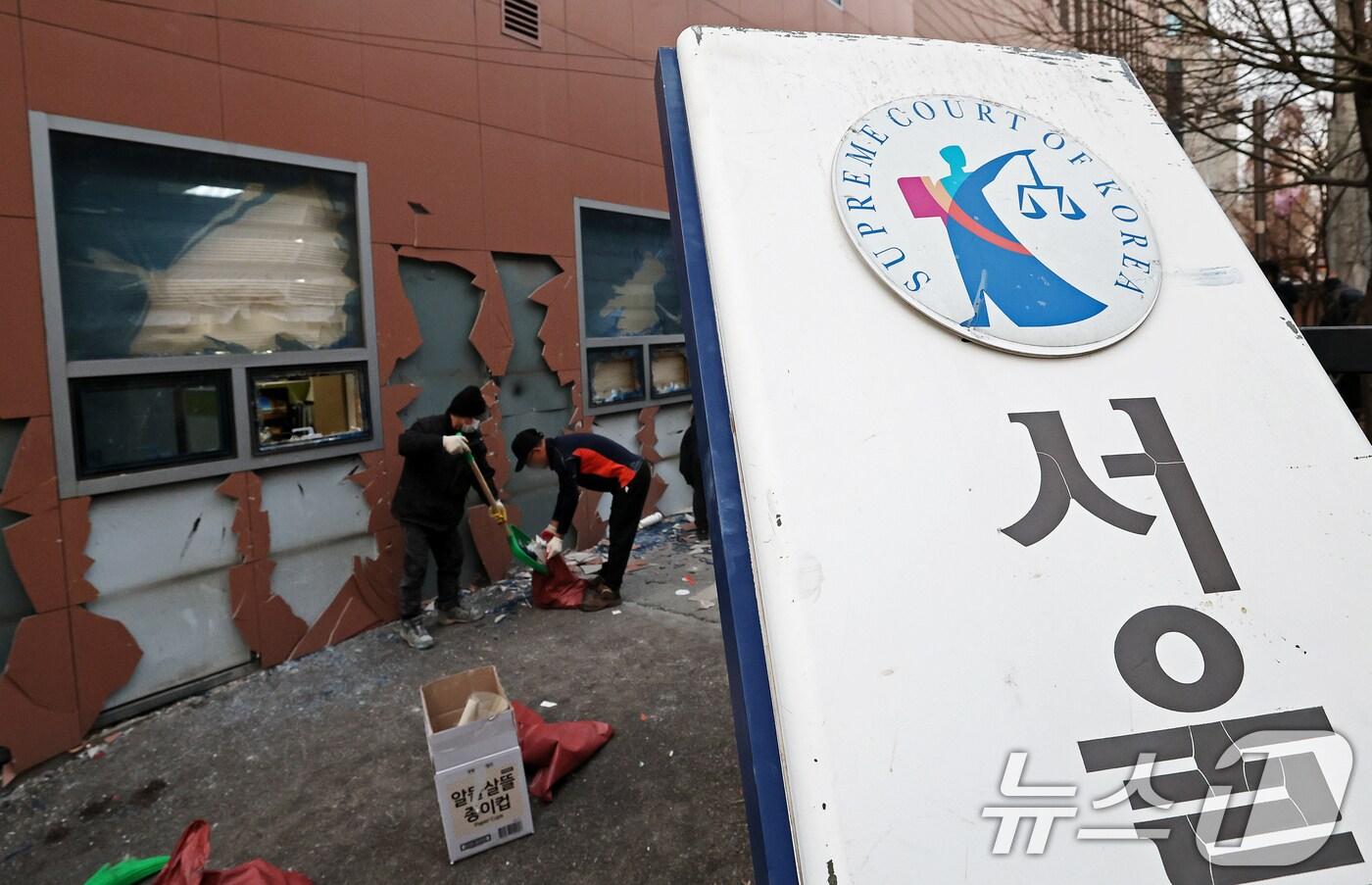 19일 오후 윤석열 대통령 지지자들의 폭력 난입 사태가 발생한 서울 마포구 서울서부지방법원 후문의 기울어진 법원 현판 뒤에서 관계자들이 폐기물을 치우고 있다. 2025.1.19/뉴스1 ⓒ News1 오대일 기자
