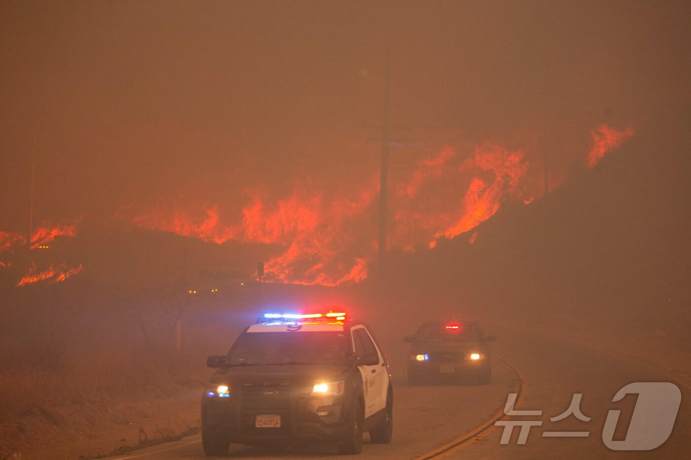 본문 이미지 - 22일(현지시간) 미국 캘리포니아주 로스앤젤레스 북서부 샌타클라리타 근처 캐스테익 호수 인근에서 휴스 산불이 발생한 가운데, 경찰차들이 산불 현장 인근을 지나가고 있다. 2025.01.22 ⓒ 로이터=뉴스1 ⓒ News1 김지완 기자
