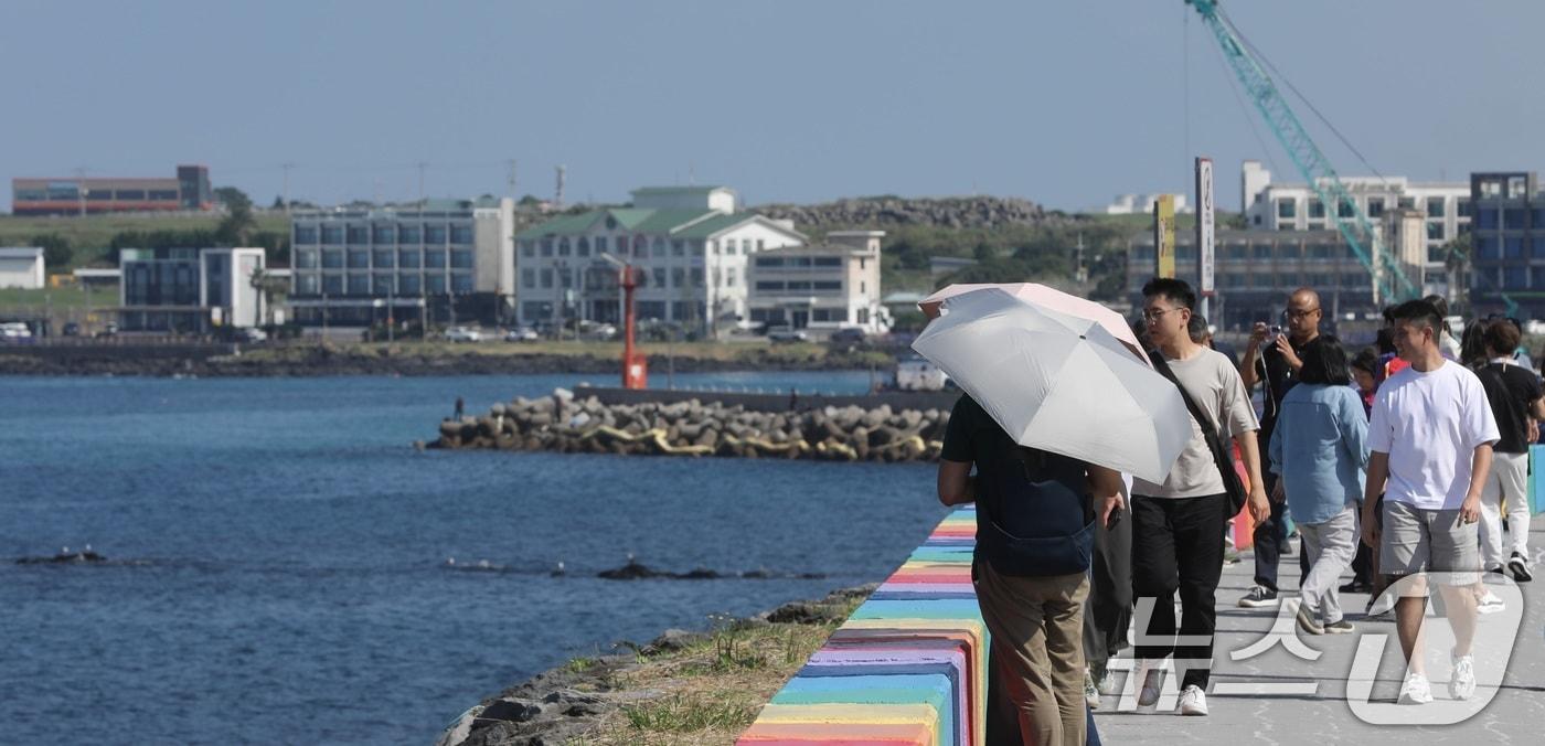 12일 오후 제주시 용담 해안도로에서 양산과 반팔 차림을 한 관광객들이 제주의 풍광을 즐기고 있다. 제주는 10월에도 낮 기온이 29~30도의 무더운 날씨를 보이고 있다. 2025.10.12/뉴스1 ⓒ News1 고동명 기자