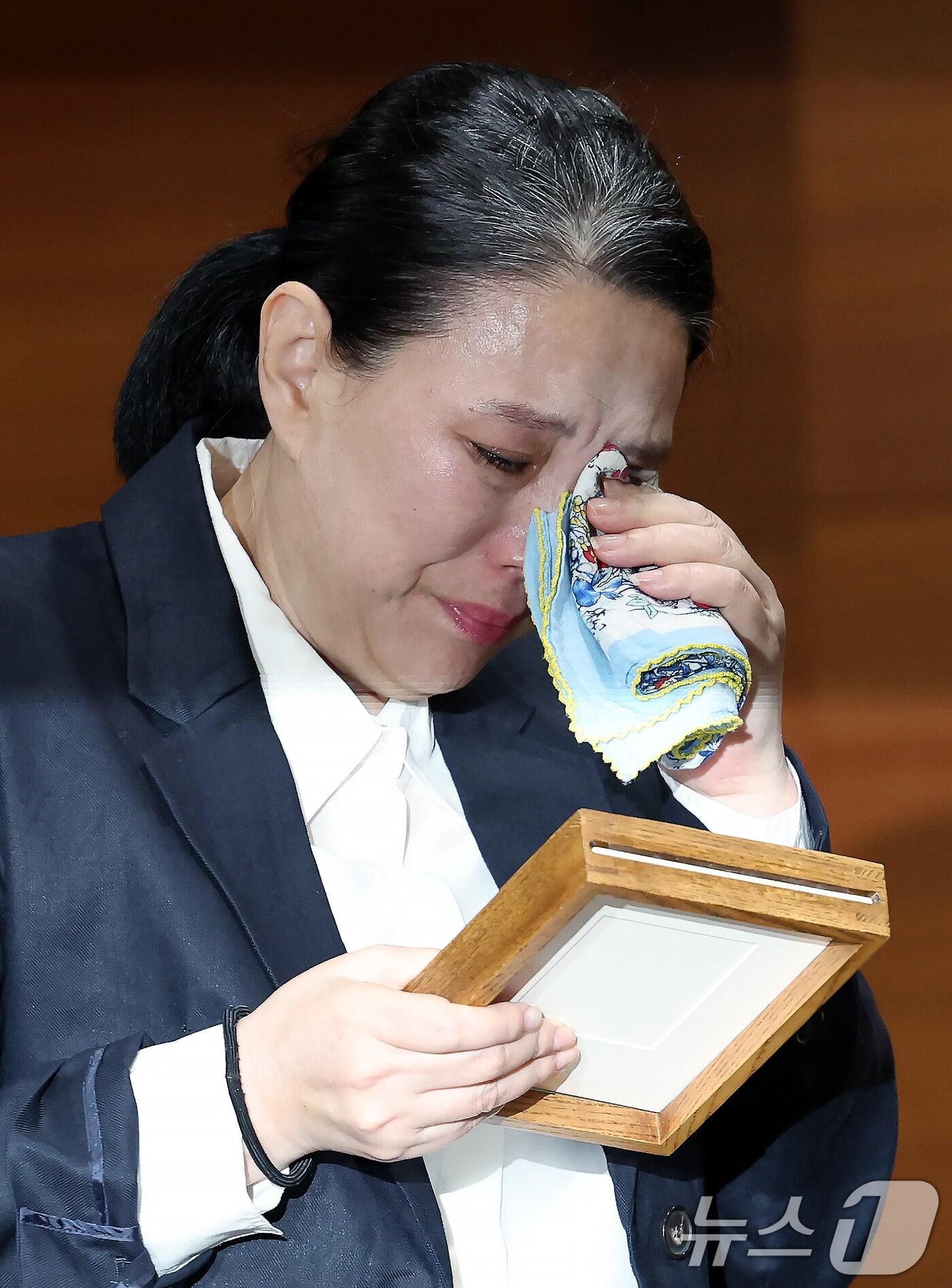 본문 이미지 - 직장 내 괴롭힘을 호소하며 스스로 목숨을 끊은 MBC 기상캐스터 오요안나 씨의 어머니 장연미 씨가 15일 오전 서울시 마포구 상암동 MBC 상암사옥 골든마우스홀에서 열린 MBC-고 오요안나 유족 기자회견에서 안형준 MBC 사장에게 받은 고인의 명예 사원증을 바라보며 눈물을 훔치고 있다. ⓒ News1 박정호 기자