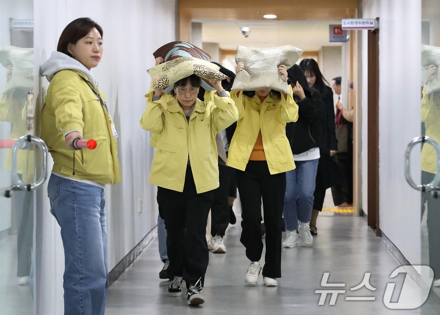 본문 이미지 - 대구 달서구청에서 지진 발생 상황을 가정해 열린 대피 훈련에서 구청 직원들이 지진 대피 안내방송에 따라 방석으로 머리를 보호하며 인근 대피소로 이동하고 있다. 2025.10.28/뉴스1 ⓒ News1 공정식 기자