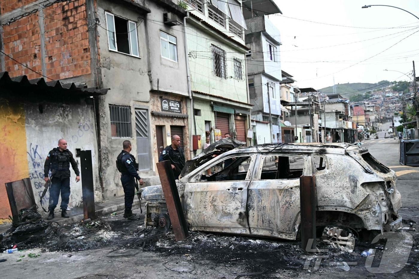 28일&#40;현지시간&#41; 브라질 리우데자네이루 페냐에서 봉쇄 작전 중 설치된 바리케이드의 일부였던 불탄 차량 옆에 경찰관들이 서 있다. 2025.10.28. ⓒ AFP=뉴스1 ⓒ News1 이정환 기자