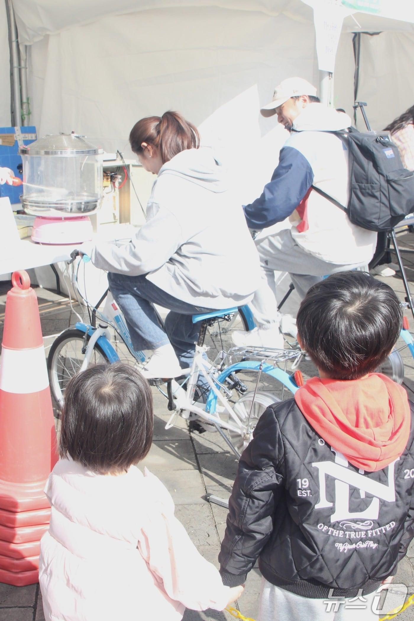 본문 이미지 - 1일 제주시 신상공원에서 열린 제5회 제주 환경교육한마당에서 두 자녀를 둔 부부가 자전거 페달을 돌려 솜사탕을 만들고 있다./뉴스1 