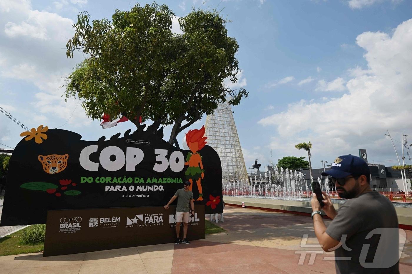 9일(현지시간) 브라질 파라 주 벨렘에서 한 관광객이 COP30 마스코트 쿠루피라가 그려진 현수막을 들고 사진을 찍고 있다. 2025.11.09. ⓒ AFP=뉴스1 ⓒ News1 이정환 기자