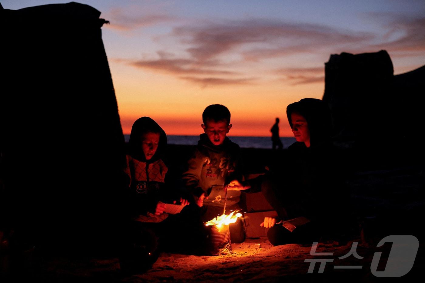 17일&#40;현지시간&#41; 팔레스타인 가자지구에서 어린이들이 모닥불 옆에 앉아 온기를 쬐고 있다. 2025.11.17. ⓒ 로이터=뉴스1 ⓒ News1 윤다정 기자