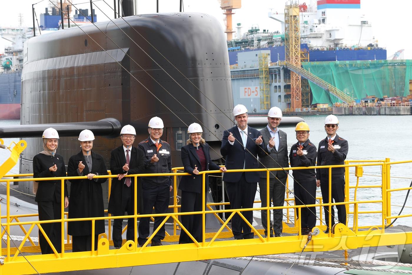 멜라니 졸리 캐나다 산업부 장관(가운데)이 지난달 24일 한화오션 거제사업장에서 김희철 한화오션 대표이사(왼쪽 네 번째), 강환석 방위사업청 차장(왼쪽 세 번째) 등과 함께 한화오션이 건조한 잠수함인 장영실함을 배경으로 단체사진을 찍고 있다. (한화오션 제공. 재판매 및 DB 금지) 2025.11.24/뉴스1