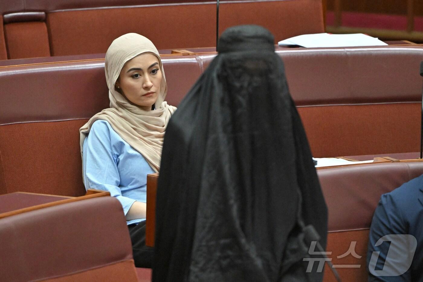 24일(현지시간) 호주 캔버라 상원 본회의장에서 파티마 패이먼 무소속 상원의원(왼쪽)이 극우 정당 '원 네이션'의 대표인 폴린 핸슨 상원의원이 이슬람 복장인 부르카를 착용한 모습을 지켜보고 있다. 핸슨 의원은 공공장소에서 부르카 및 기타 얼굴 가리개 착용을 금지하는 법안 제출이 막히자 이에 대한 항의의 표시로 부르카를 착용했다. 2025.11.24 ⓒ 로이터=뉴스1 ⓒ News1 김지완 기자