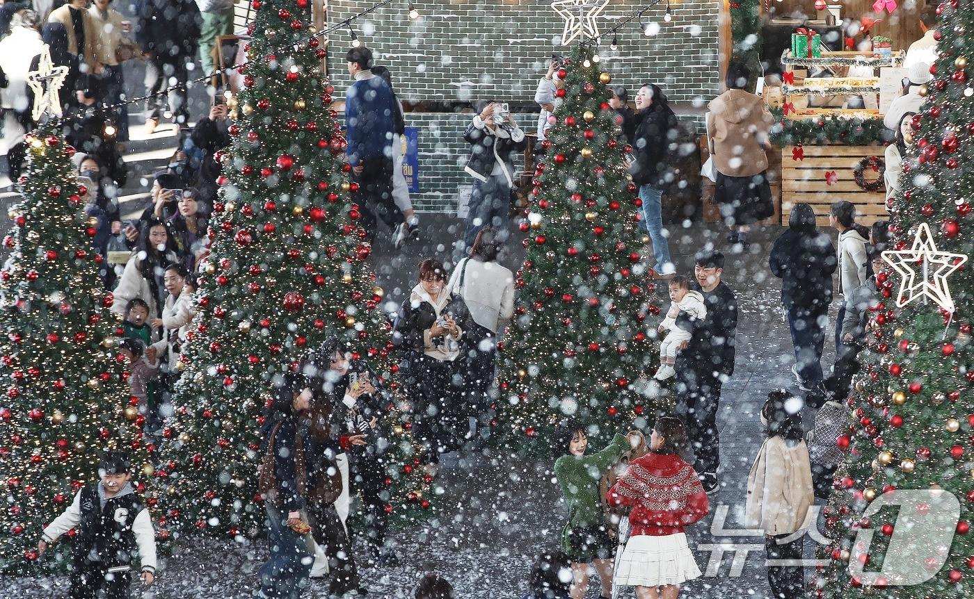 27일 부산 해운대구 영화의전당에서 열린 &#39;크리스마스 빌리지 부산 2025&#39;를 찾은 시민들이 인공눈을 맞으며 크리스마스 트리를 배경으로 사진을 찍는 등 겨울 분위기를 즐기고 있다. 2025.11.27/뉴스1 ⓒ News1 윤일지 기자