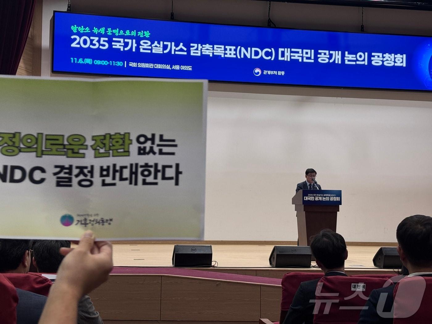 본문 이미지 - 6일 서울 영등포구 국회의원회관 대회의실에서 열린 2035 국가온실가스 감축목표 대국민 공개 논의 공청회에서 김성환 장관이 발언 중인 가운데 환경단체 회원들이 손피켓을 들어보이고 있다. 기후에너지환경부는 2035년 국가온실가스감축목표&#40;NDC&#41;를 2018년 대비 50~60% 감축 범위에서 확정할 예정이다. 2025.11.6/뉴스1 ⓒ News1 황덕현 기후환경전문기자