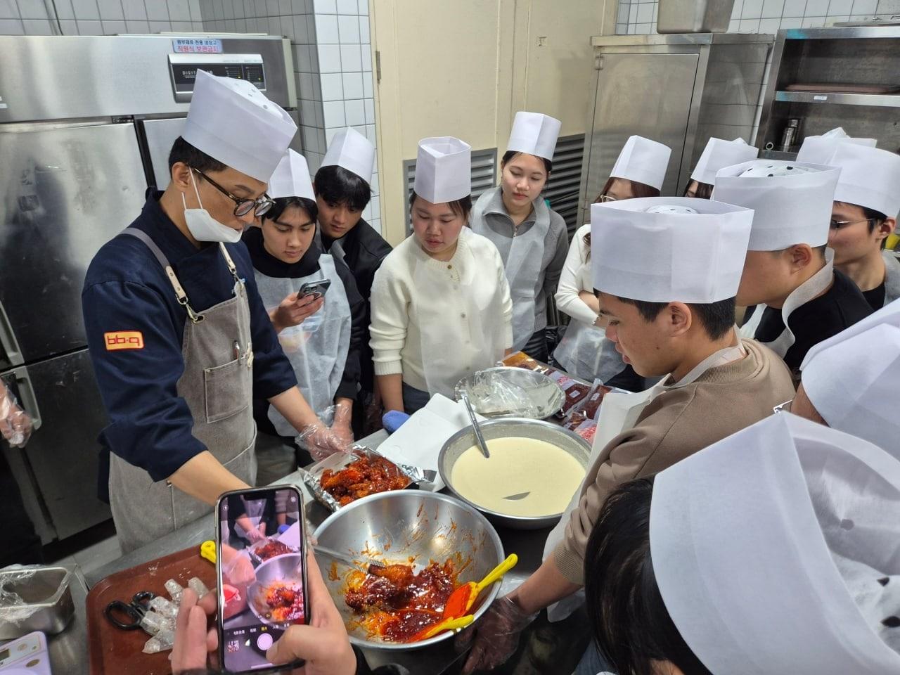 본문 이미지 - 경기도 이천에 위치한 BBQ 치킨대학을 찾은 조선대 글로벌학부 외국인 유학생들이 치킨 조리법에 대한 설명을 듣는 모습,&#40;BBQ 제공&#41;