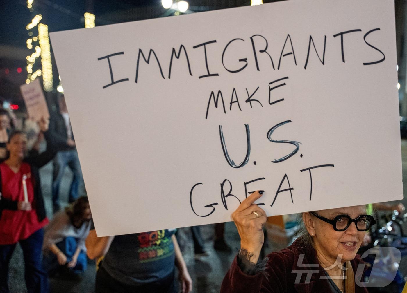 본문 이미지 - 18일, 미국 루이지애나주 뉴올리언스에서 이민자 인권 운동가들이 이민세관집행국(ICE) 요원들을 피해 피난처를 찾는 이민자들을 지지하는 시위를 벌이던 중 한 여성이 피켓을 들고 잇다. 2025.12.19. ⓒ 로이터=뉴스1