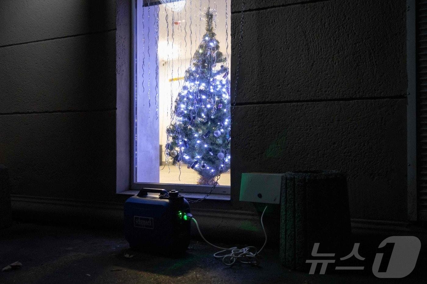 22일(현지시간) 우크라이나 남부 도시 오데사에서 러시아의 미사일과 드론 공격으로 에너지 시설이 파괴돼 정전이 이어지는 가운데 한 주택 앞에 발전기가 놓여 있고 크리스마스 트리가 장식돼 있다.2025.12.22.ⓒ AFP=뉴스1