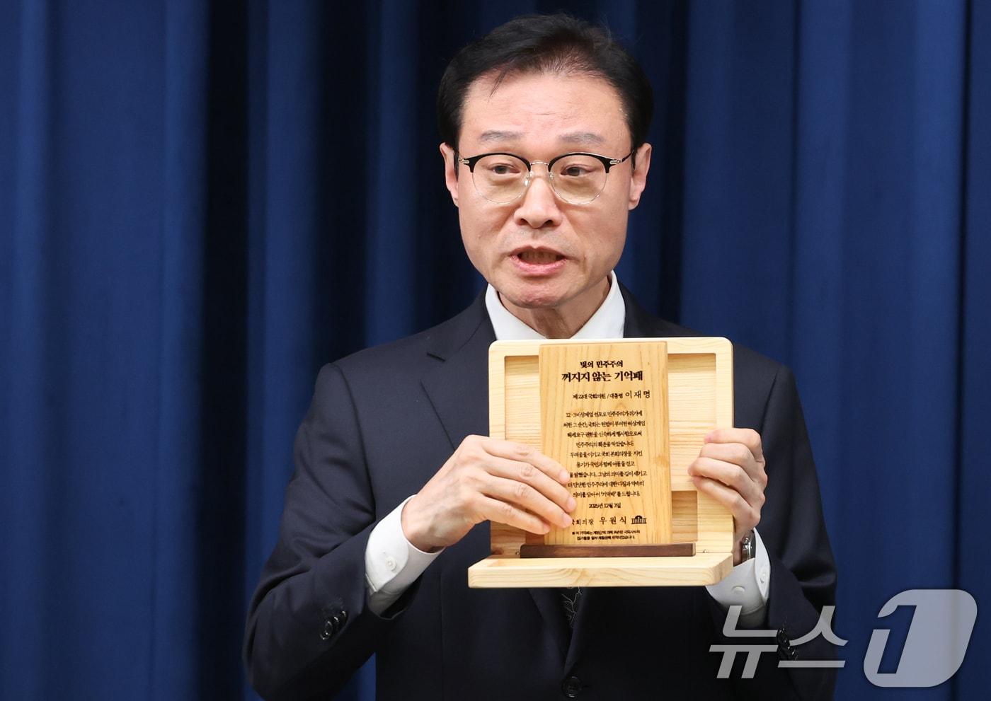 이규연 홍보소통수석이 3일 서울 용산 대통령실 청사에서 열린 5부 요인 초청 오찬 관련 브리핑에서 &#39;빛의 민주주의 꺼지지 않는 기억패&#39;를 들어보이고 있다. 이재명 대통령은 이날 오찬에서 우원식 국회의장으로부터 지난해 12월 3일 계엄군에 의해 부서졌던 국회 집기들을 재활용해 만든 &#39;기억패&#39;를 전달 받았다. 2025.12.3/뉴스1 ⓒ News1 허경 기자