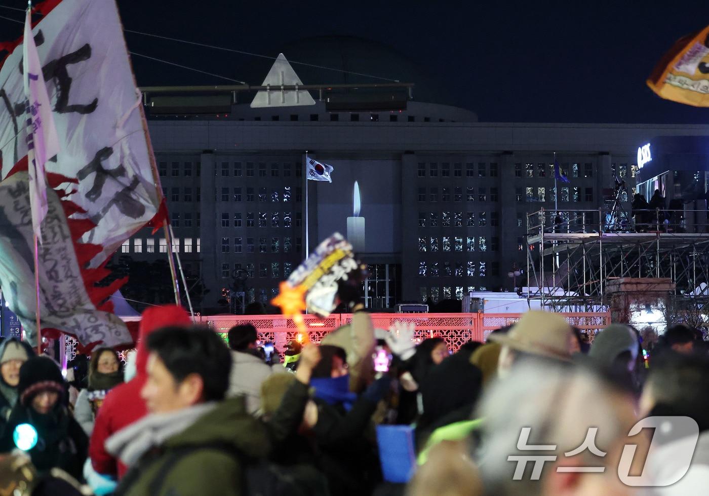 12·3 비상계엄 1년을 맞아 서울 국회의사당 외벽에 계엄 해제 당시를 되새기는 ‘미디어 파사드’가 펼쳐지고 있다. 화면에는 촛불 하나가 켜진 장면이 연출되고 있고 국회 밖에서는 시민들이 행진을 이어가고 있다. 2025.12.3/뉴스1 ⓒ News1 박지혜 기자