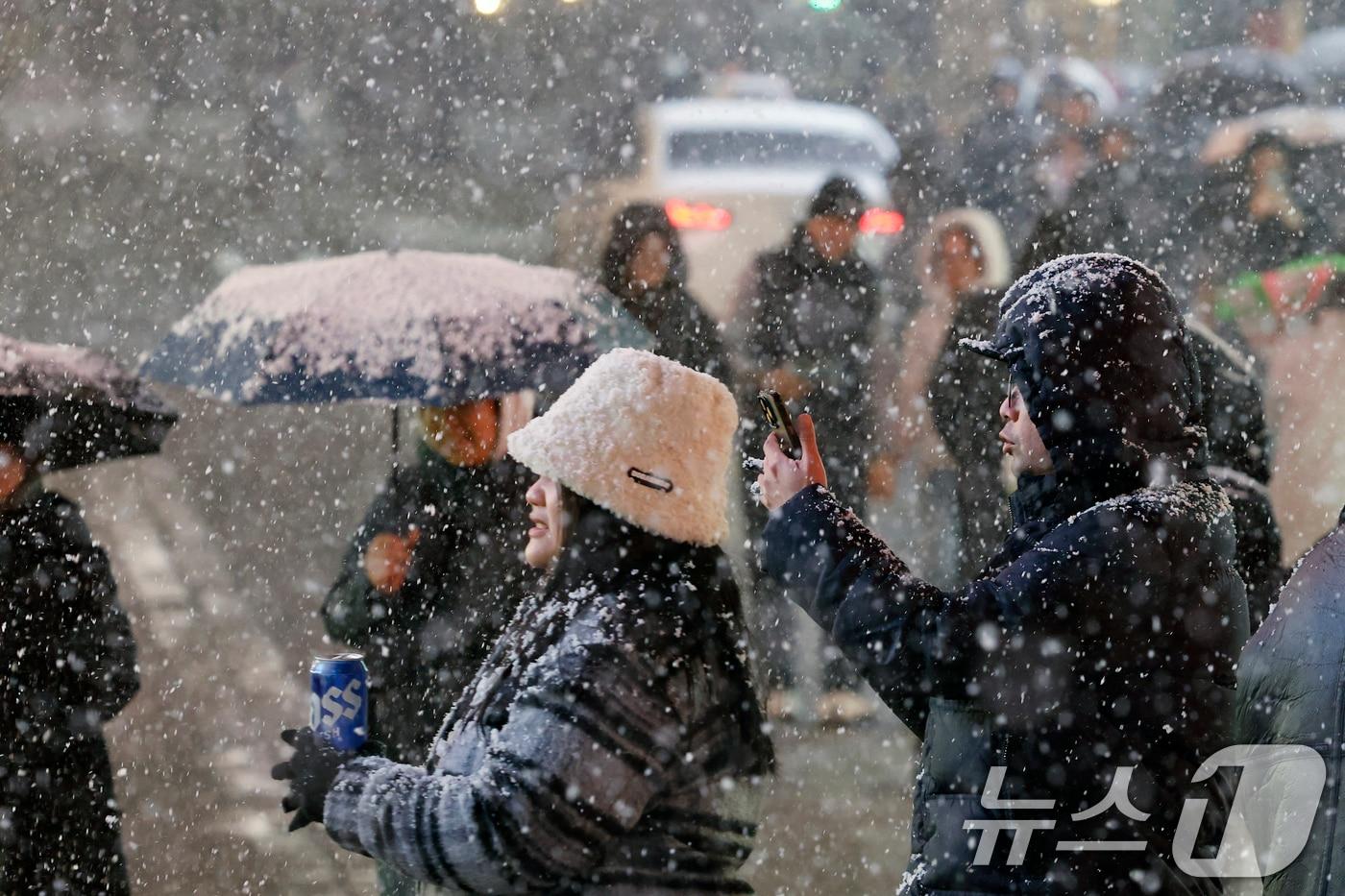 첫눈이 내린 4일 오후 서울 중구 명동을 찾은 관광객들이 내리는 눈을 맞으며 즐거운 시간을 보내고 있다. 기상청은 &#34;퇴근 시간대 강한 눈이 내릴 가능성이 크다＂며 동네 예보와 실시간 날씨를 확인할 것을 당부했다. 2025.12.4/뉴스1 ⓒ News1 박정호 기자