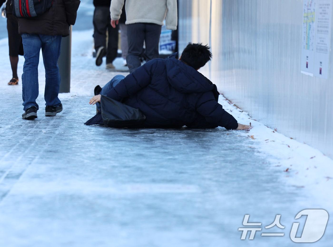 본문 이미지 - 폭설 후 한파로 도로 곳곳이 얼어붙은 5일 오전 서울 광화문역 일대에서 한 시민이 빙판길에 미끄러져 넘어지고 있다. 2025.12.5/뉴스1 ⓒ News1 구윤성 기자
