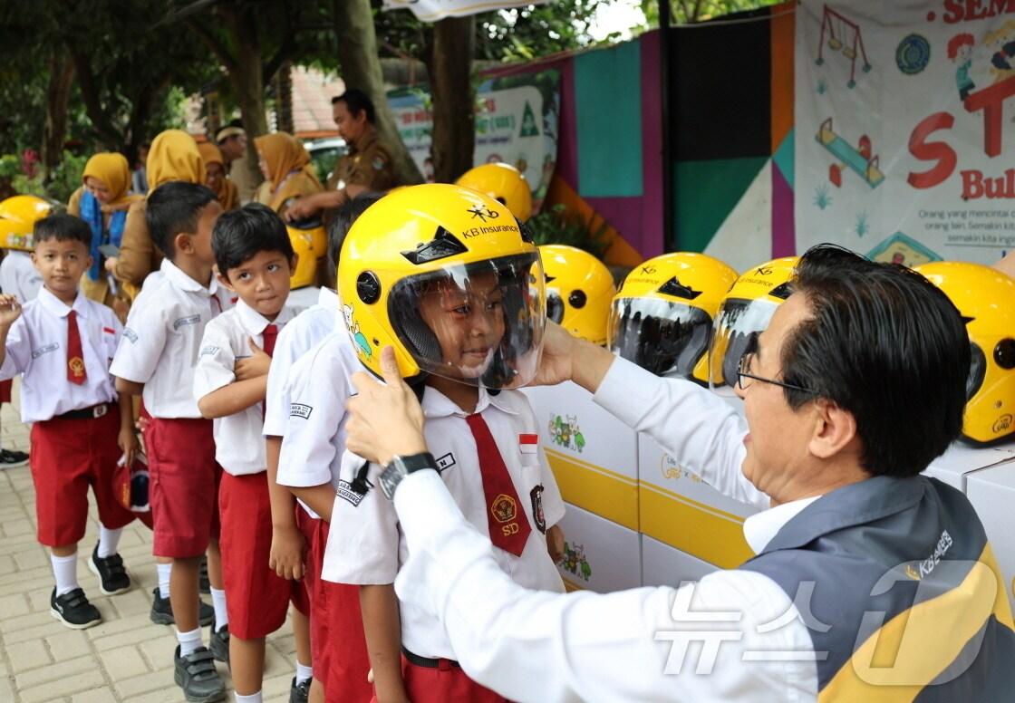 본문 이미지 - KB손해보험은 지난 11일, 인도네시아 자카르타 서부 지역에 위치한 발라라자(Balaraja) 초등학교에서 ‘이륜차 안전모 전달식’을 진행했다. 이날 안전모 전달식에 참여한 KB손해보험 조정래 인니법인장이 학생들에게 안전모를 씌워주고 있다./사진제공=KB손해보험