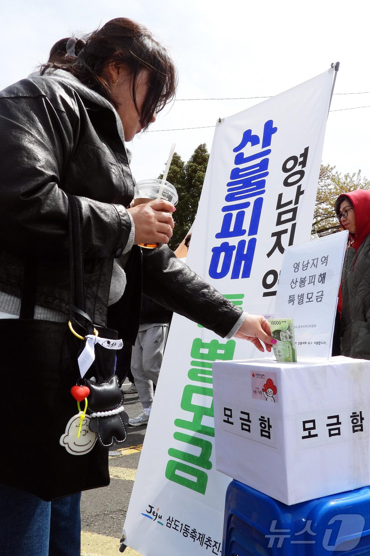 본문 이미지 - 30일 오후 제주시 삼도1동 전농로 일대에서 열린 &#39;제18회 전농로 왕벚꽃 축제&#39;에서 한 상춘객이 영남지역 산불피해 지원 특별모금함에 성금을 넣고 있다. 2025.3.30/뉴스1 ⓒ News1 오미란 기자