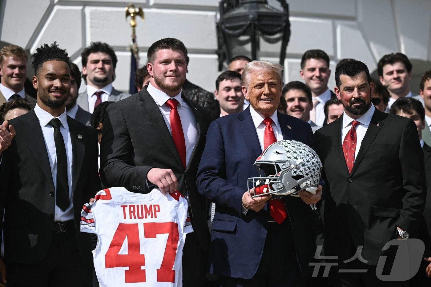 본문 이미지 - 도널드 트럼프 미국 대통령이 14일(현지 시간) 워싱턴 백악관에서 열린 2025 대학풋볼 내셔널리그 챔피언인 오하이오 주립대 풋볼팀 선수들과 기념 행사서 챔피언십 트로피와 유니폼를 들고 포즈를 취하고 있다. 2025.04.15 ⓒ AFP=뉴스1 ⓒ News1 우동명 기자