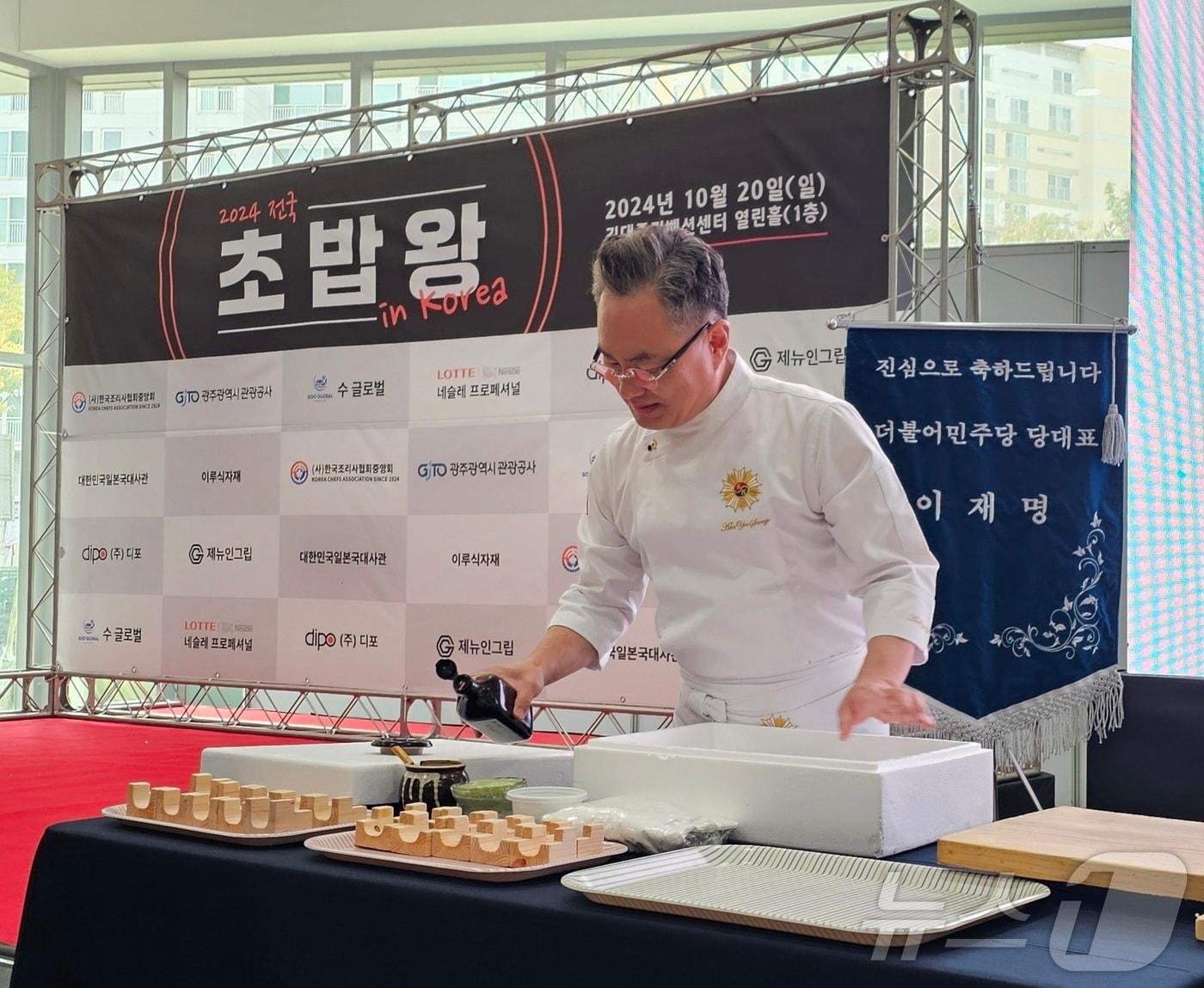 본문 이미지 - 2024년 10월 20일 김대중컨벤션센터에서 ‘전국초밥왕대회’를 개최한 안유성 조리명장이 1㎏당 30만 원에 달하는 자연산 다금바리 초밥 시연을 준비하고 있다. 뒤편엔 이재명 당시 더불어민주당 대표의 축하기가 놓였다. ⓒ News1 서충섭 기자