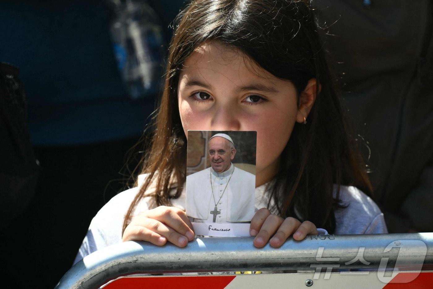 본문 이미지 - 프란치스코 교황의 장례 미사에서 한 여성 어린이가 프란치스코 교황 사진을 들고 있는 모습. ⓒ AFP=뉴스1