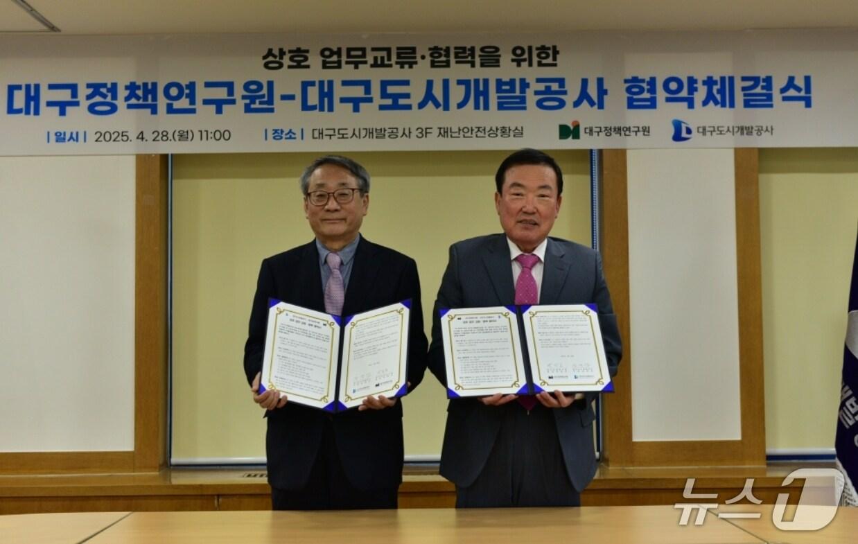 본문 이미지 - 정명섭 대구도시개발공사 사장(오른쪽)과 박양호 대구정책연구원장이 업무교류 및 협력을 위한 협약을 체결한 뒤 협약서를 펼쳐 보이고 있다.(대구도시개발공사 제공. 재판매 및 DB 금지)