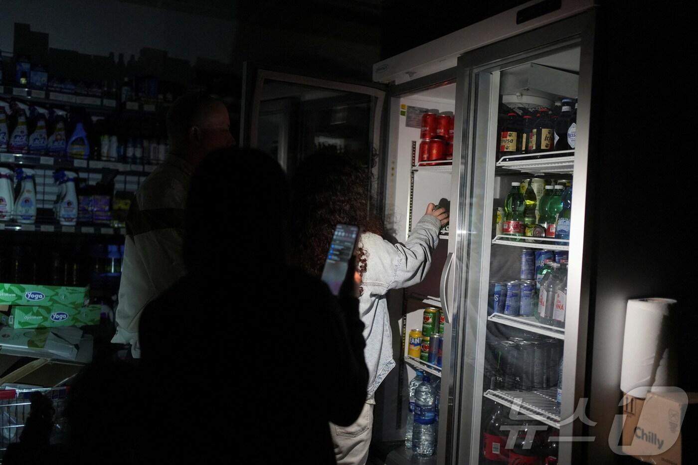 28일(현지시간) 스페인 바르셀로나의 한 마트에서 사람들이 물건을 사기 위해 휴대전화로 빛을 비추고 있다. 2025.04.28 ⓒ 로이터=뉴스1 ⓒ News1 정지윤 기자