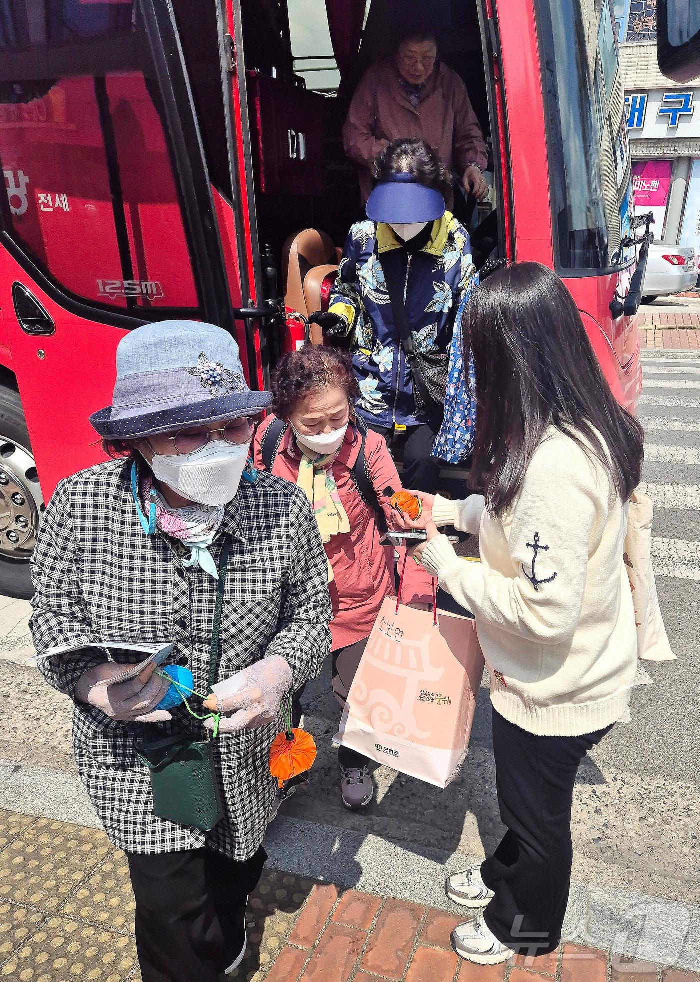 본문 이미지 - 3일 대구시티투어버스를 이용해 군위전통시장을 찾은 관광객이 군위군 관계자가 나눠주는 장바구니와 시장 맛집 리플릿을 받고 있다. (군위군 제공우ㅣ