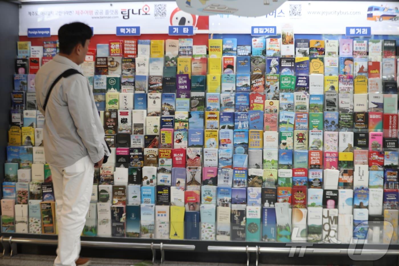 본문 이미지 -  제주국제공항 진열대에 진열된 제주관광지 홍보물을 살펴보는 관광객. 2025.5.1 ⓒ 뉴스1 강승남 기자