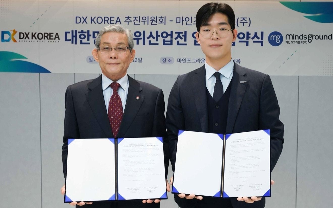 본문 이미지 - 민환기 마인즈그라운드 대표(사진 오른쪽)와 김영후 DX KOREA 2026 추진위원장이 12일 대한민국 방위산업전(DX KOREA) 2026 업무협약을 체결했다.(마인즈그라운드 제공)