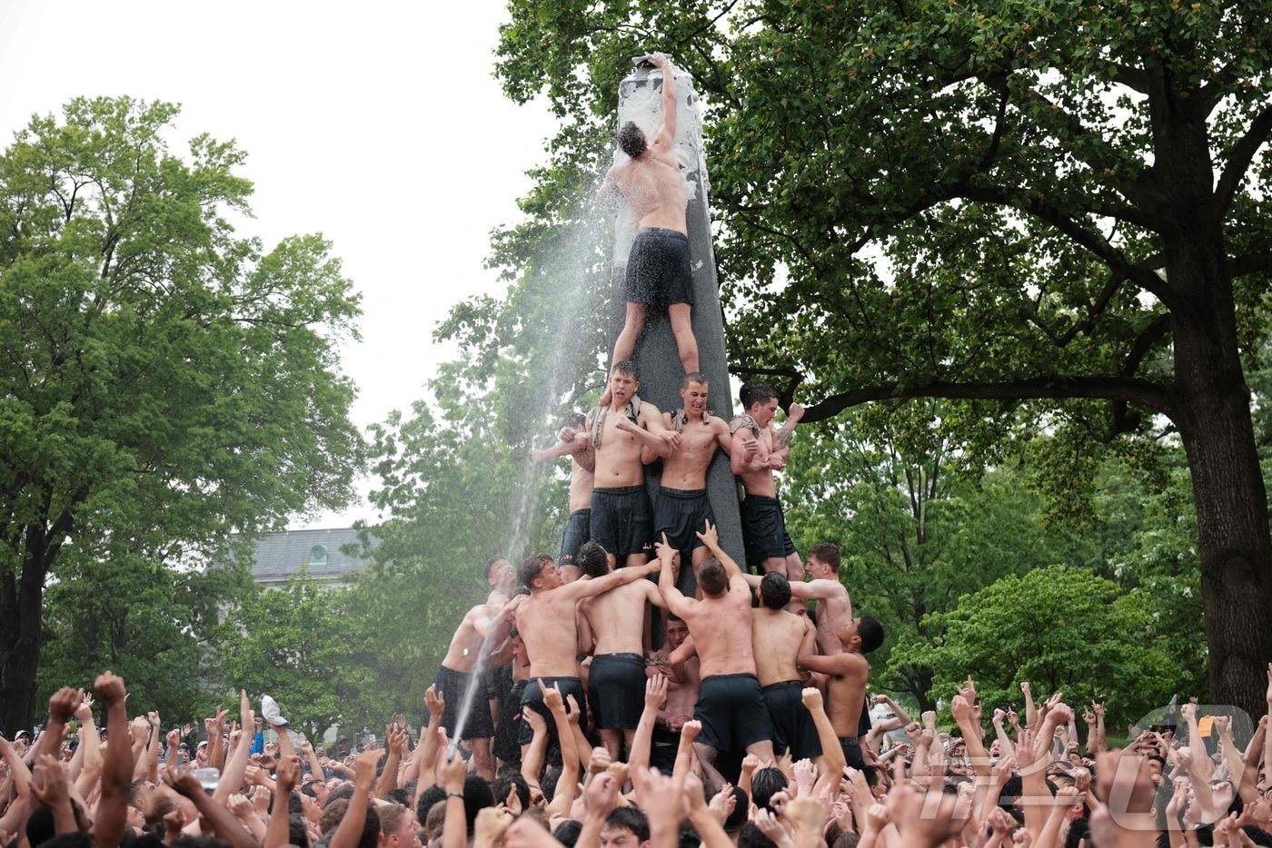 미국 해군사관학교에서 사관생도들이 14일(현지시간) 미국 메릴랜드 주 아나폴리스 미 해군 사관학교에서 '딕시 컵'을 떨어뜨리기 위해 인간 피라미드를 만들어 헌던 기념물 꼭대기에 오르고 있다.  ⓒ AFP=뉴스1