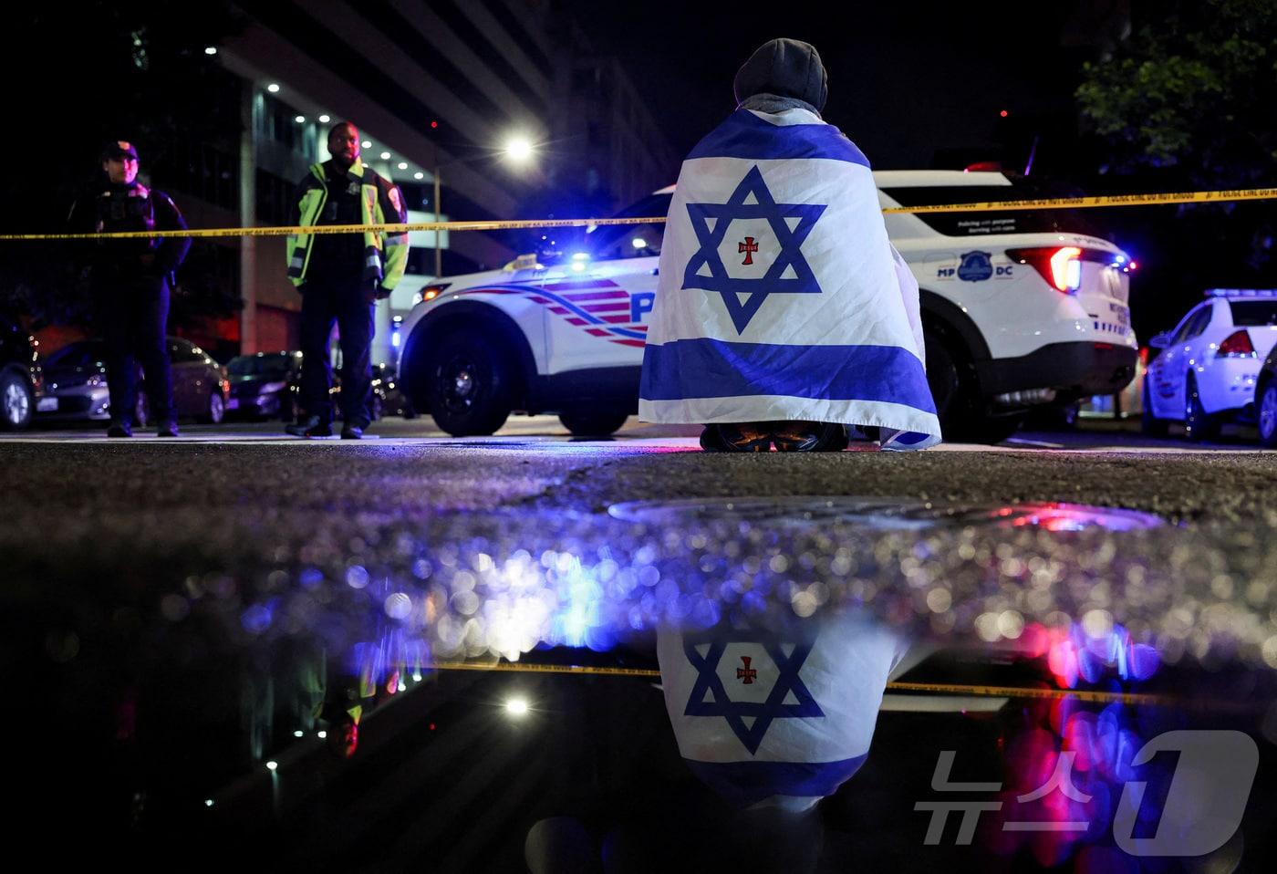 주미 이스라엘 대사관 직원 2명이 21일(현지시간) 워싱턴 DC에 있는 수도 유대인 박물관 인근에서 총에 맞아 사망한 가운데 이스라엘 국기를 망토로 두른 한 남성이 수사를 벌이고 있는 경찰을 지켜보고 있다. 2025.05.21 ⓒ 로이터=뉴스1 ⓒ News1 최종일 선임기자