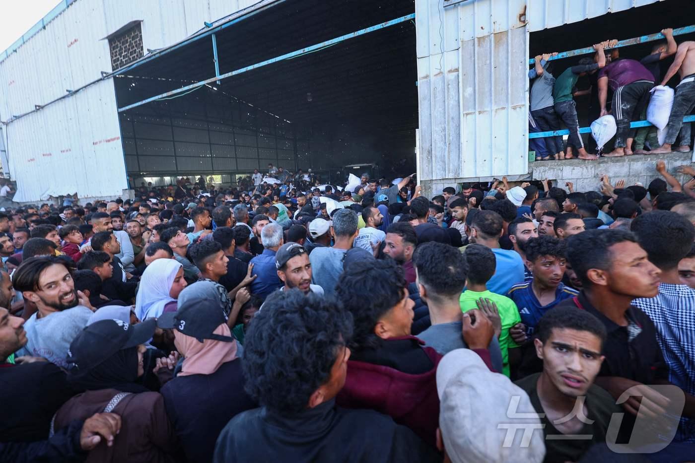 28일(현지시간) 가자지구 중부 데이르 엘발라에 있는 세계식량계획(WFP) 창고를 습격해 구호 식량 자루를 나르고 있는 팔레스타인 가자인들. 두달 넘게 이스라엘에 의해 봉쇄되어 있던 이들은 유엔이 개설했던 많은 배급소 대신 이스라엘과 미국이 단 두 곳의 배급소만 열자 제대로 구호품을 받지 못했다.2025.05.28. ⓒ AFP= 뉴스1