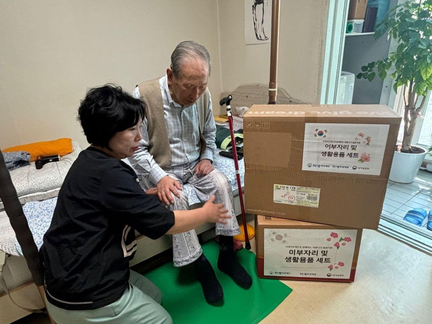 본문 이미지 - 자생의료재단 관계자가 독립유공자 어르신 가정을 방문해 여름 침구류 세트와 생필품을 전달하고 있다.(자생한방병원 제공)