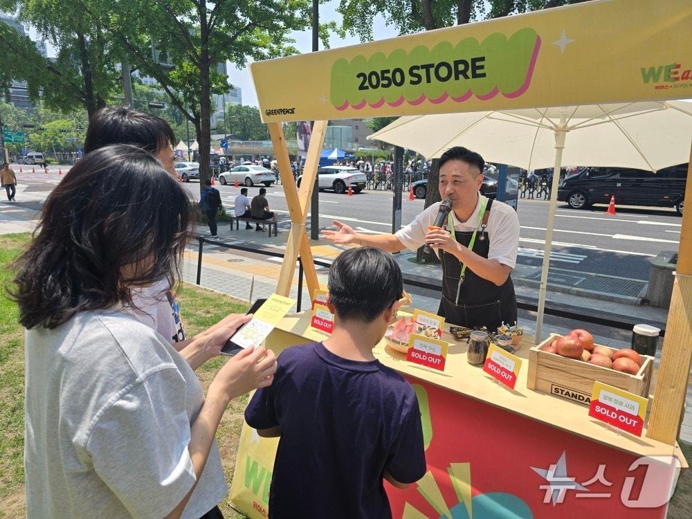 본문 이미지 - 1일 정상훈 그린피스 선임 캠페이너가 2050년에는 구매하기 어렵거나 비쌀 것으로 예상되는 사과, 전복 등이 전시된 부스에서 시민에게 탄소중립에 대해 설명하고 있다. ⓒ 뉴스1 황덕현 기자