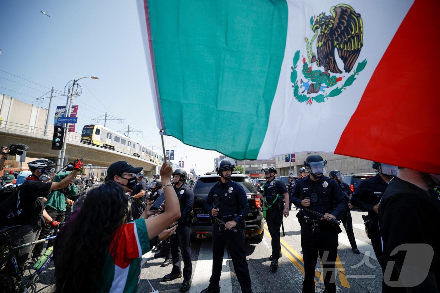 8일(현지시간) 미국 캘리포니아주 로스앤젤레스(LA)에서 이민 당국의 대규모 불법 이민자 단속에 반대하는 시위대가 경찰 앞에서 멕시코 국기를 흔들고 있다. 2025.06.08 ⓒ 로이터=뉴스1 ⓒ News1 김지완 기자