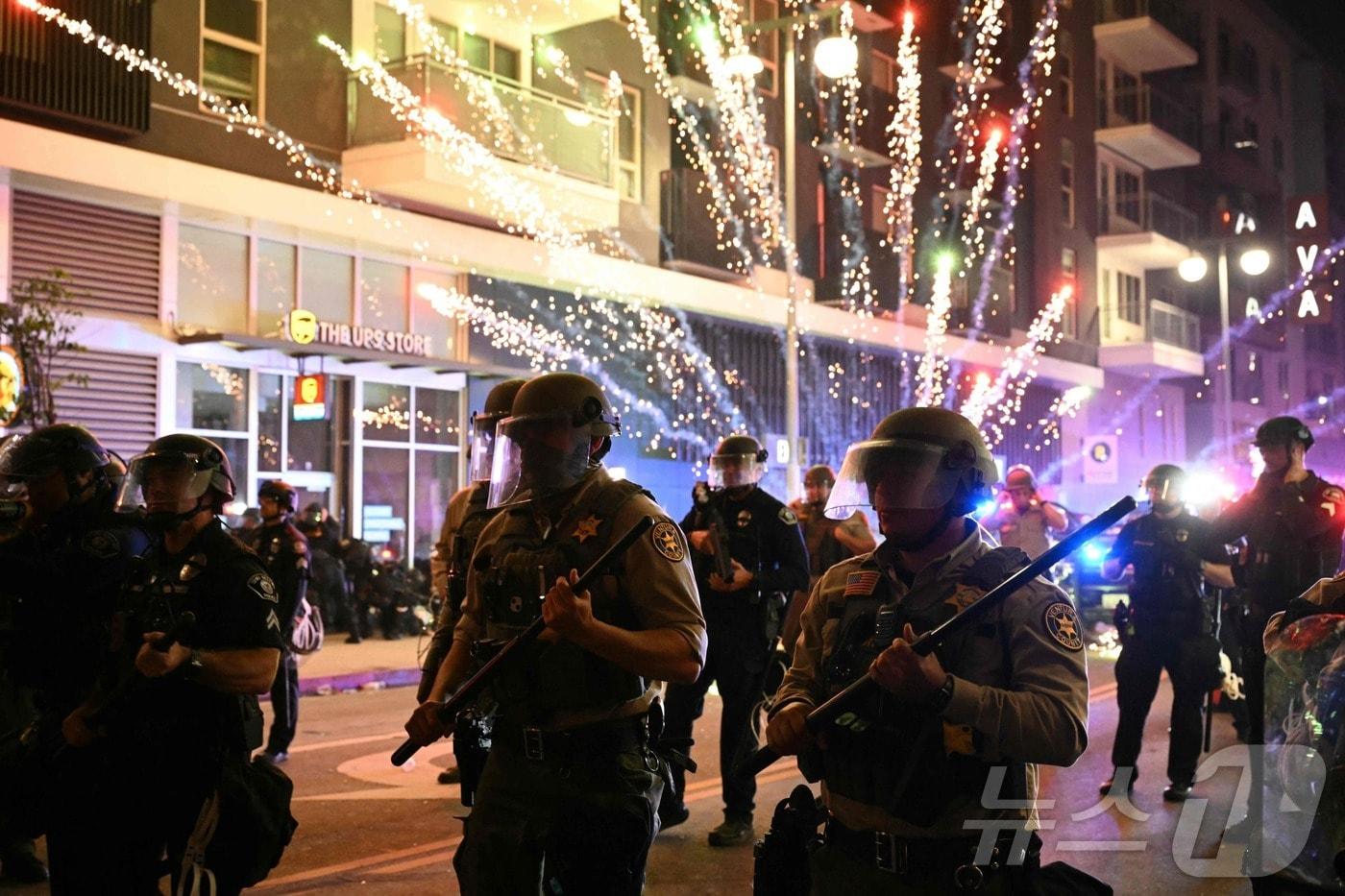 2025년 6월 9일 로스앤젤레스(LA) 시내 리틀 도쿄 인근에서 연방 이민단속 작전에 대응하는 시위 도중 진압 장비를 착용한 벤투라 카운티 보안관 사무실 소속 대원들 뒤로 폭죽이 터지고 있다.  ⓒ AFP=뉴스1 ⓒ News1 신기림 기자