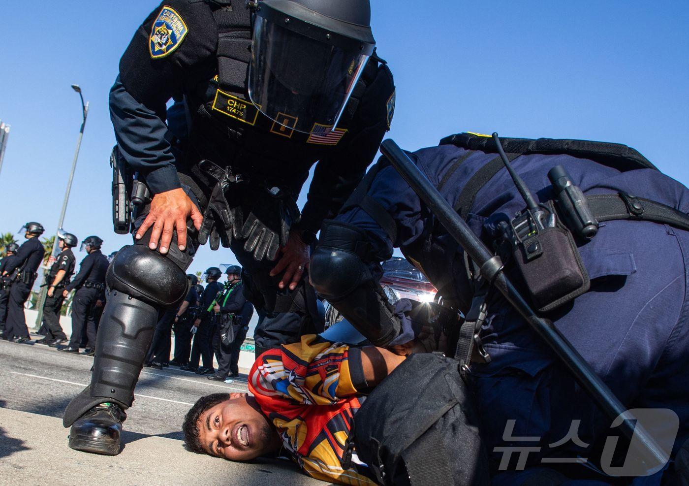 지난 달 10일(현지시간) 미국 캘리포니아 로스앤젤레스(LA)에서 연방 당국의 이민 단속 조치에 항의하는 시위가 계속되는 가운데 캘리포니아 고속도로 순찰대원이 101 프리웨이 고가도로에서 시위 참가자를 체포하는 모습. ⓒ AFP=뉴스1 ⓒ News1 최종일 선임기자