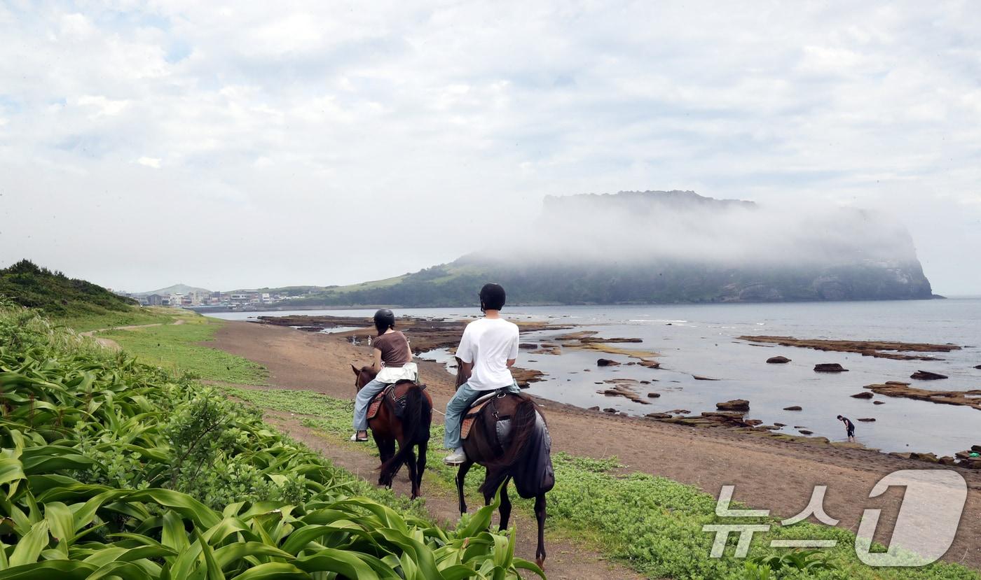 본문 이미지 - 1제주 서귀포시 성산읍 광치기해변에서 관광객들이 해무 낀 성산일출봉을 배경으로 승마체험을 하고 있다. 2025.6.19 ⓒ 뉴스1 