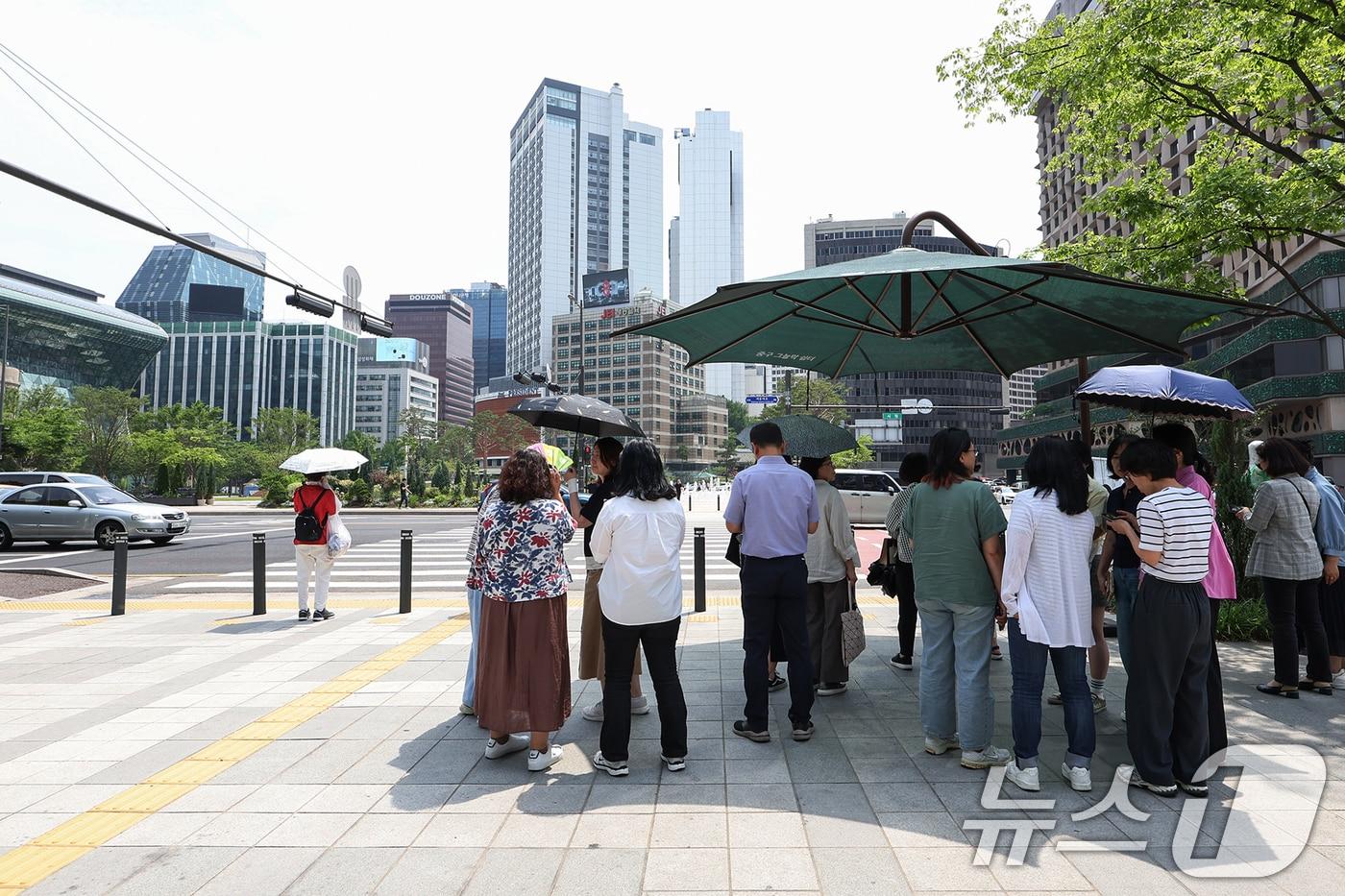서울 지역 낮 최고 기온이 32도까지 올라 무더위가 찾아온 19일 서울중구 서울시청 앞 횡단보도 앞에서 시민들이 그늘막 아래 모여 따가운 햇빛을 피하고 있다. 2025.6.19/뉴스1 ⓒ News1 민경석 기자