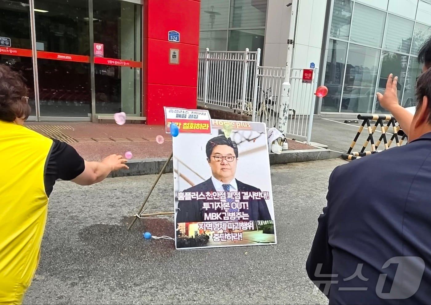 2025년 6월 2일 천안시 동남구 홈플러스 천안점 앞에서 열린 폐점 반대 기자회견에서 한 참가자가 던진 물풍선에 김병주 MBK파트너스 회장 얼굴 사진이 부착된 입간판이 넘어지고 있다. 2025.6.2/뉴스1 ⓒ News1 이시우 기자