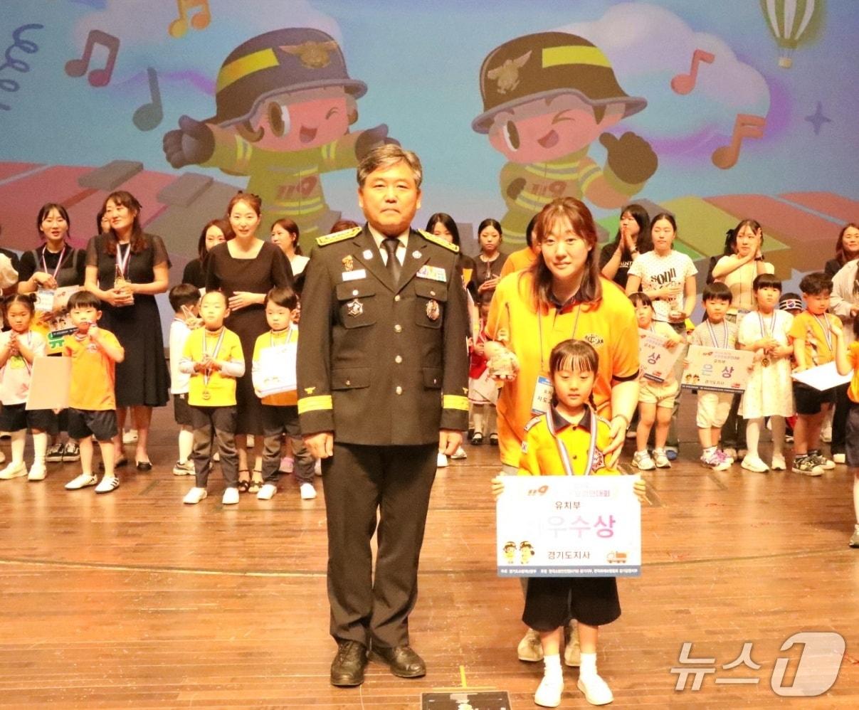 본문 이미지 - 지난 19일 경기아트센터 대극장에서 열린 '제26회 경기도 119 소방동요 경연대회'에 참가한 안산 드리머하나어린이집이 최우수상 수상한 후 최덕호 경기도소방재난본부 생활안전담당관(왼쪽)과 기념촬영을 하고 있다. (안산소방서 제공. 재판매 및 DB 금지) 2025.6.20/뉴스1