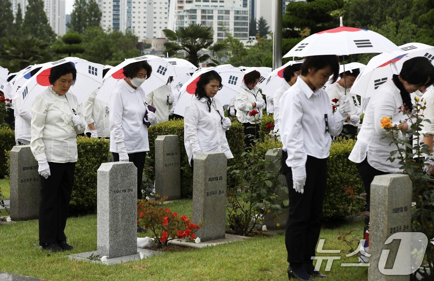 25일 오전 부산 남구 유엔기념공원에서 열린 제75주년 6·25전쟁 참전 유엔전몰용사 추모제에서 태극기 우산을 쓴 참석자들이 유엔군 전몰장병 묘역에 헌화한 뒤 묵념하고 있다. 2025.6.25/뉴스1 ⓒ News1 윤일지 기자