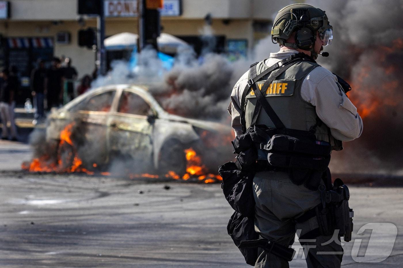 미국 이민세관단속국&#40;ICE&#41;이 지난 6월 7일&#40;현지시간&#41; 캘리포니아주 로스앤젤레스 카운티의 파라마운트에서 불법 체류자 체포 후 시위대와 경찰이 대치하는 가운데 도로 위 불타는 차량에서 연기가 피어오르고 있다. 2025.6.7./뉴스1 ⓒ 로이터=뉴스1 ⓒ News1 이창규 기자