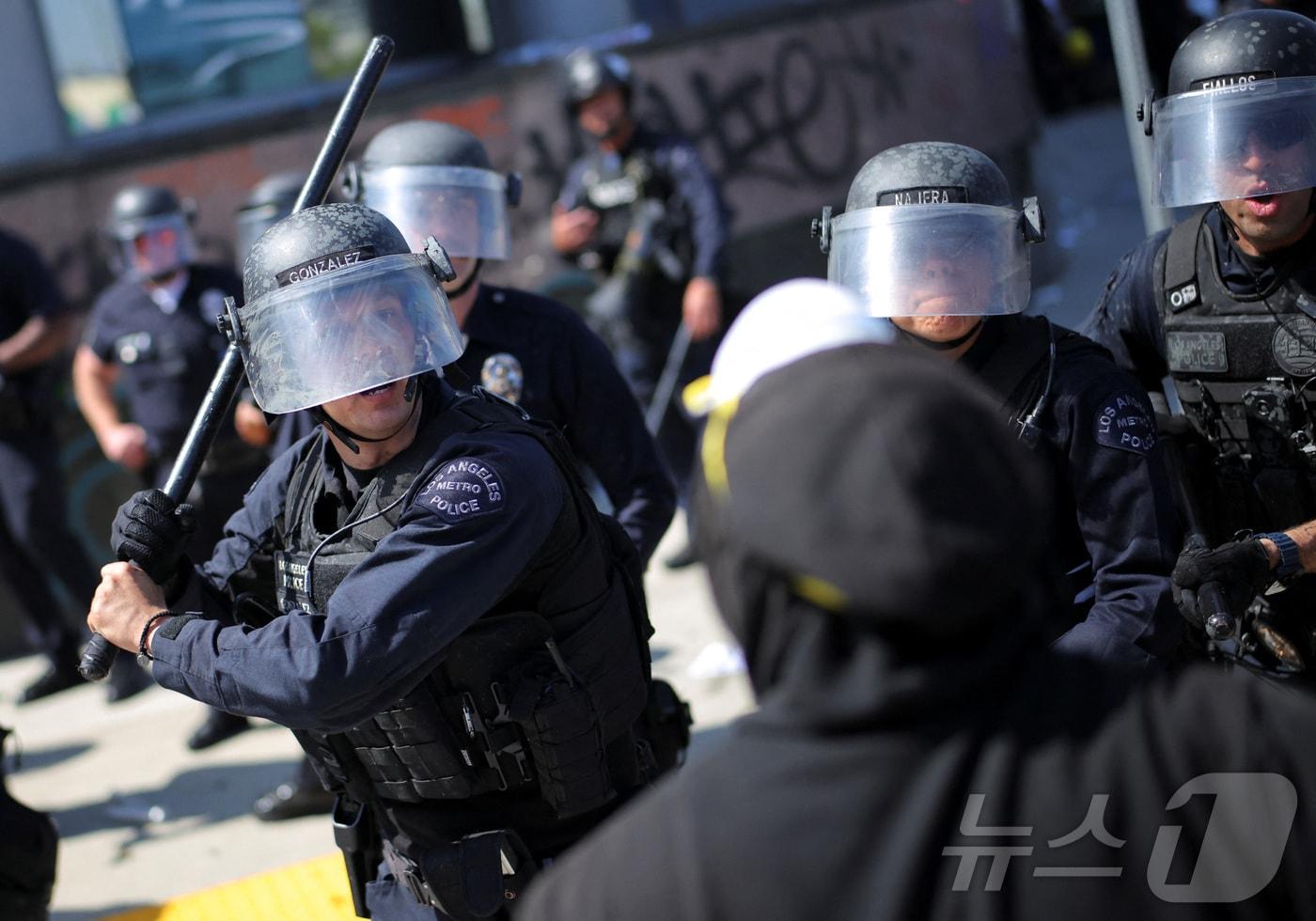 미국 캘리포니아주 로스앤젤레스 경찰관이 2025년 6월 8일 미국 캘리포니아 로스앤젤레스 시내에서 연방 이민 단속에 반대하는 시위 중 시위자들과 대치하며 곤봉을 들고 있다. 2025.6.8 ⓒ 로이터=뉴스1 ⓒ News1 강민경 기자