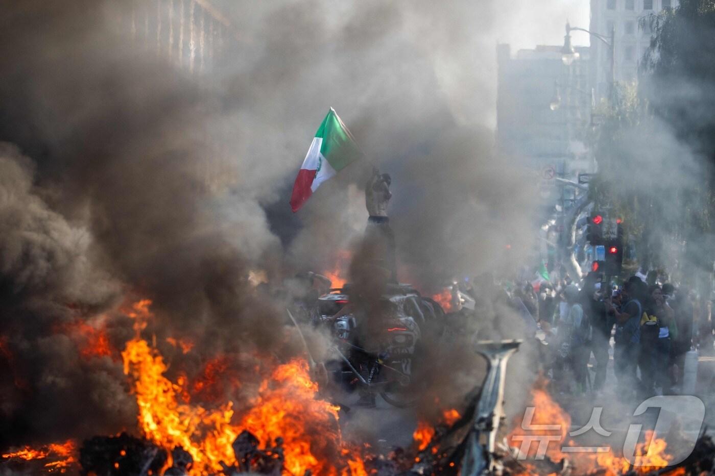 8일(현지시간) 미국 캘리포니아주 로스앤젤레스(LA)에서 한 남성이 자동차 위에 서서 멕시코 국기를 흔들고 있다. 도널드 트럼프 대통령의 행정부가 LA에서 일련의 불법 이민자 단속에 나서면서 이틀 동안 경찰, 주방위군과 시위대 사이 물리적 충돌이 이어졌다. ⓒ AFP=뉴스1 ⓒ News1 신기림 기자