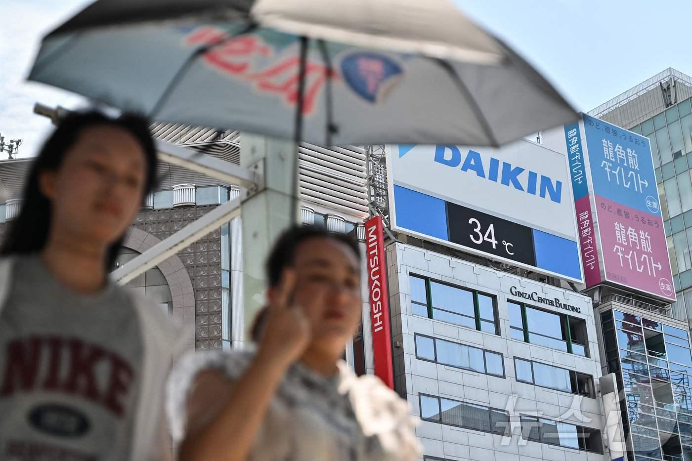 1일 양산을 쓴 시민들이 일본 도쿄 긴자 거리를 지나가고 있다. 시민들 뒤로 기온이 섭씨 34도로 표시된 전광판이 보인다. 2025.07.01 ⓒ AFP=뉴스1 ⓒ News1 김지완 기자